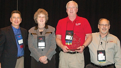 Ron Yarnell PPG Industries left and NATM President Gary Potter right present this yearrsquos NATM Green Award to Mr and Mrs Greg Snyder of Car Mate Trailers